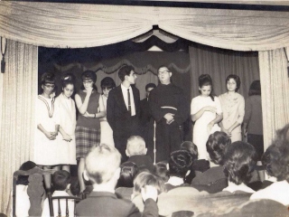 1966: Homenagem dos Congregados e Filhas de Maria do Valongo, a Frei Cosme, sob a coordenação de José Auro (em pé, de gravata, ao lado do vigário Frei Graciano). Na plateia, de costas, é possível ver a cabeça de Frei Cosme, sobressaindo do capuz da batina, bem ao lado do cordão franciscano de seu superior.